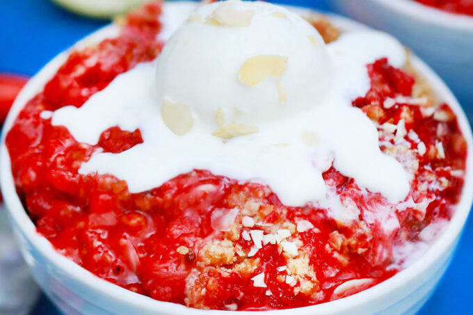 A bowl of saucy strawberry crisp topped with ice cream.