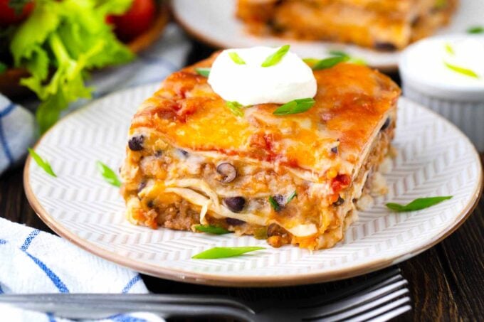 A slice of cheesy taco lasagna topped with sour cream.