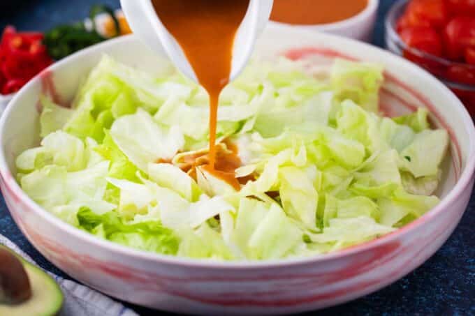 Pouring Catalina dressing over chopped lettuce in a bowl.