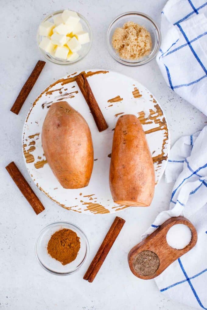 sweet potatoes on a round white board with cinnamon sugar and butter next to them