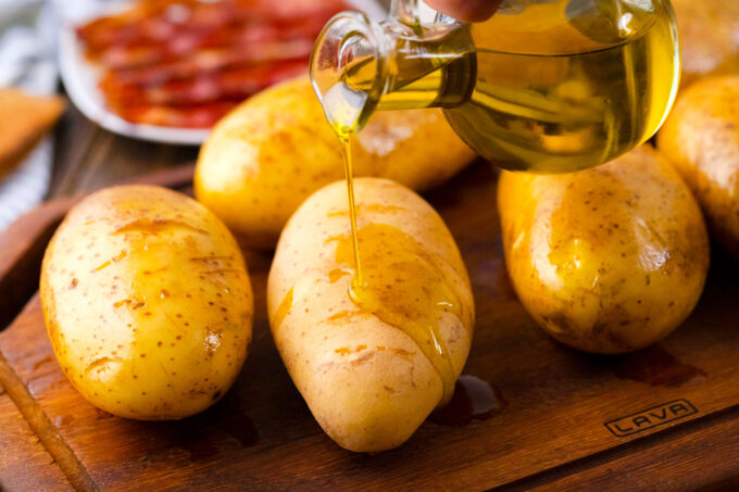 Drizzling olive oil over whole potatoes.
