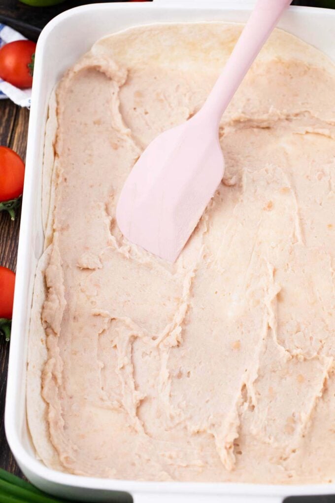Spreading a layer of refried beans in a casserole dish.