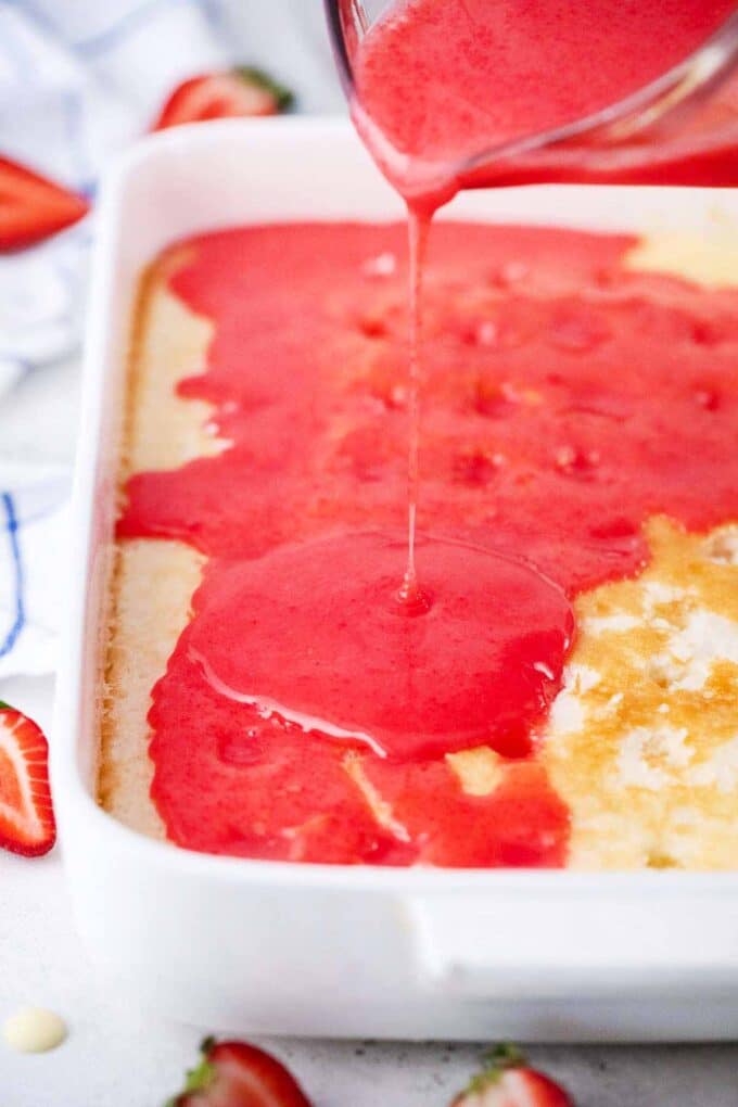 Pouring strawberry white chocolate mixture over a poked white cake