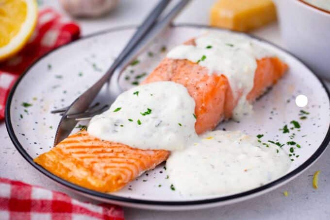 white creamy sauce for salmon on a plate on a piece of cooked salmon