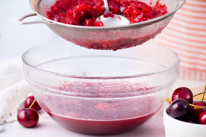 Straining cherry sauce through a fine mesh.