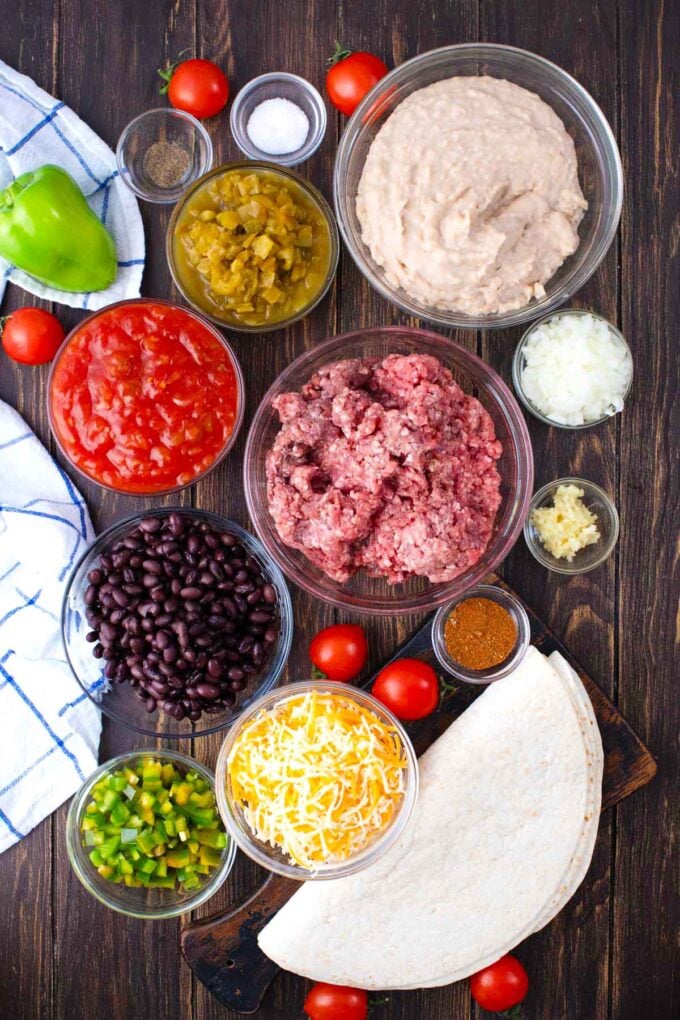Overhead shot of taco lasagna ingredients in bowls on a wooden table.