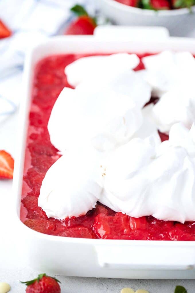 adding whipped cream on top of a strawberry poke cake