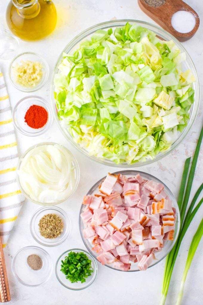 overhead shot of bacon fried cabbage ingredients in bowls on a white surface.