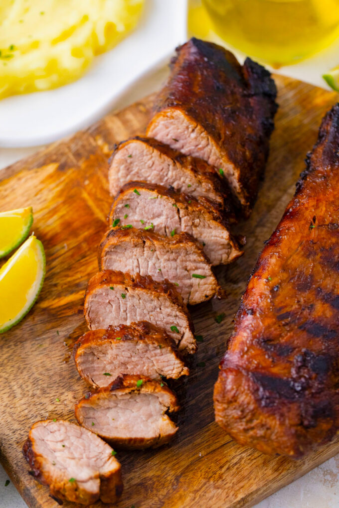 Sliced grilled pork tenderloin on a cutting board.