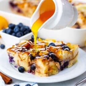 pouring honey over a baked slice of blueberry french toast casserole