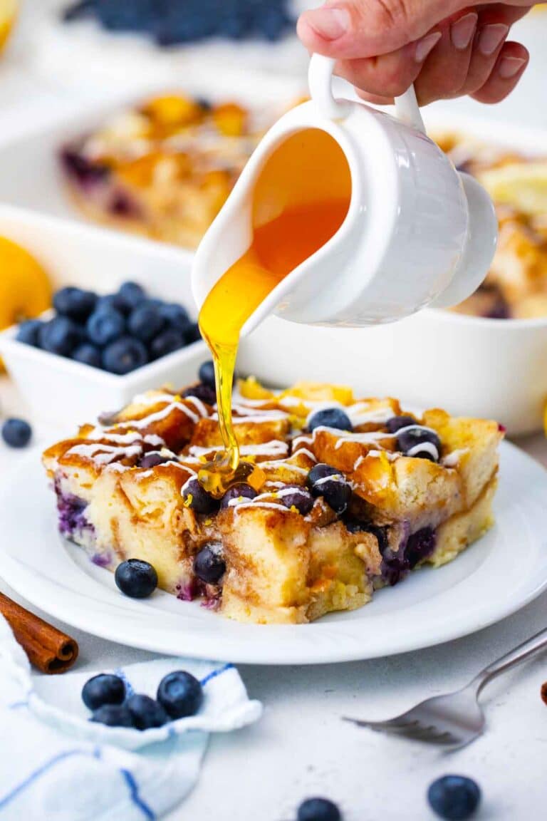 pouring honey over a baked slice of blueberry french toast casserole