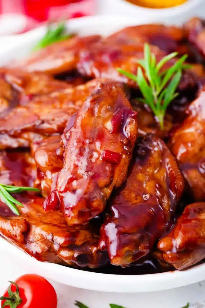 Browned and sticky boozy red wine glazed wings on a serving plate garnished with rosemary.