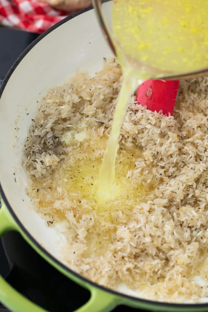 Pouring chicken broth into a skillet with rice.