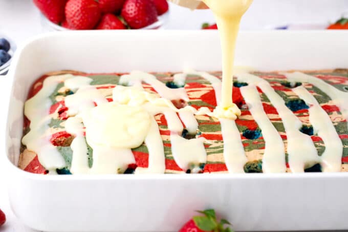 Drizzling chocolate sauce on top of poked red, white, and blue poke cake.