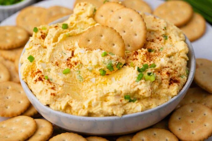 a bowl of homemade deviled eggs dip topped with paprika and chives served with crackers