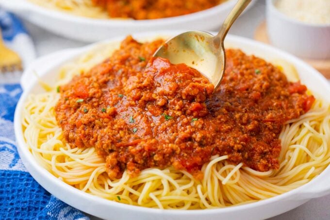 Scooping Instant Pot spaghetti sauce on top of spaghetti.