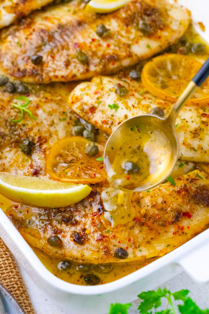 Drizzling lemon butter sauce over baked tilapia fillets.