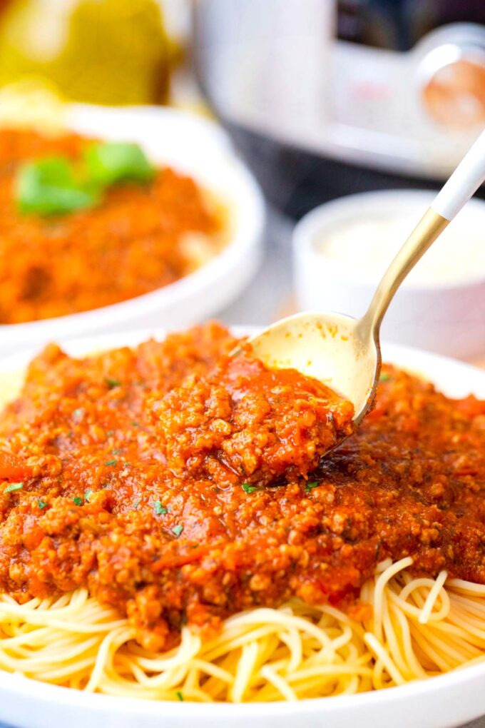 Spooning meaty homemade Instant Pot spaghetti sauce over pasta.