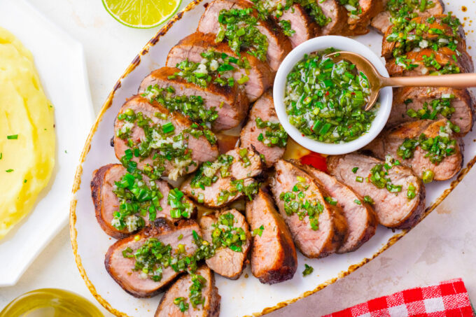 A plate of sliced grilled pork tenderloin with herby sauce.