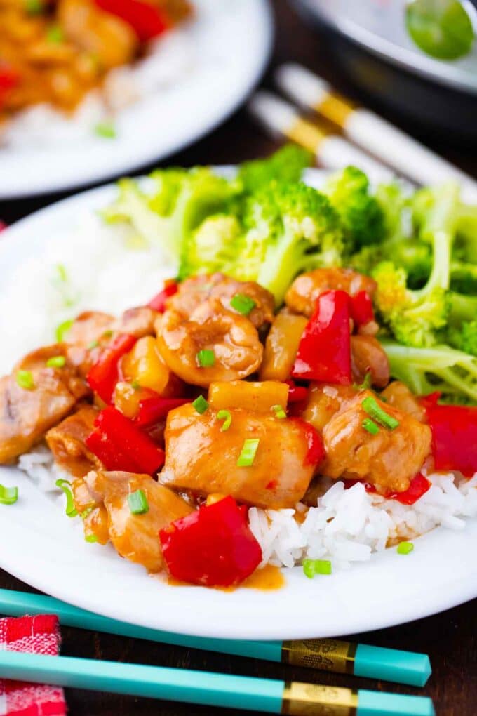 Juicy instant pot sweet and sour chicken with red bell pepper pieces and pineapple over rice and a side of broccoli.