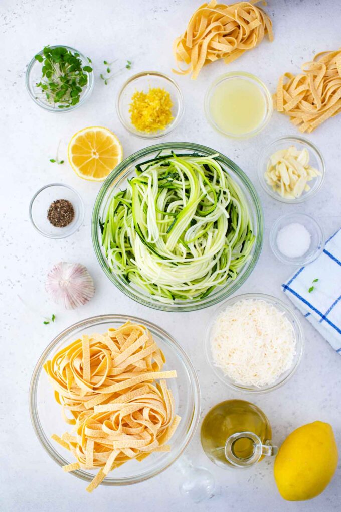 overhead shot of lemon zucchini pasta ingredients in bowls on a white surface