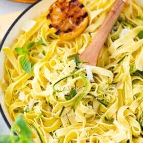 a skillet of lemon zucchini pasta topped with microgreens and grilled lemon