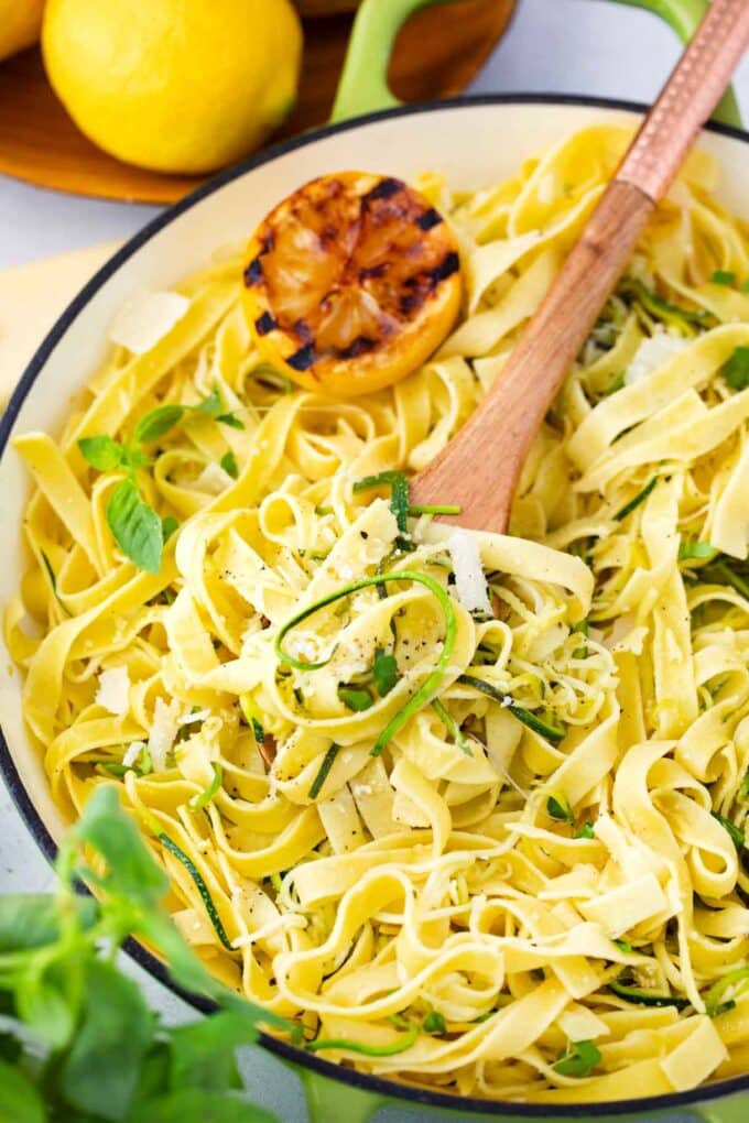 a skillet of lemon zucchini pasta topped with microgreens and grilled lemon