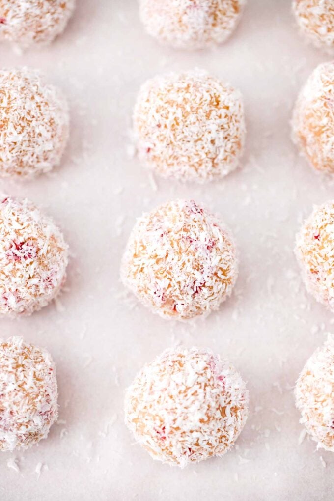 no bake strawberry coconut truffles covered in shredded coconut arranged in lines in a baking sheet