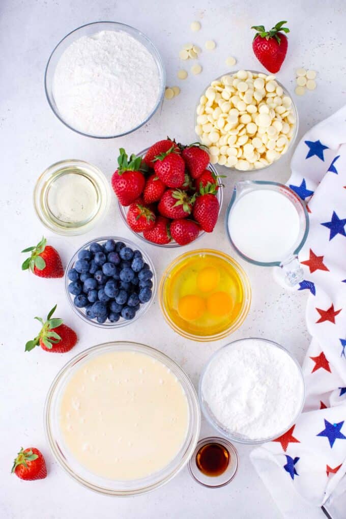 Overhead shot of patriotic poke cake ingredients in bowls on a table.