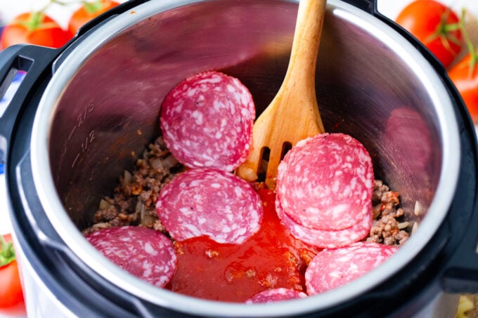 Adding tomato sauce and pepperoni to seared ground beef,