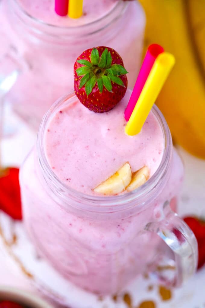 Overhead shot of creamy, pink strawberry banana smoothie, served with fresh strawberries.