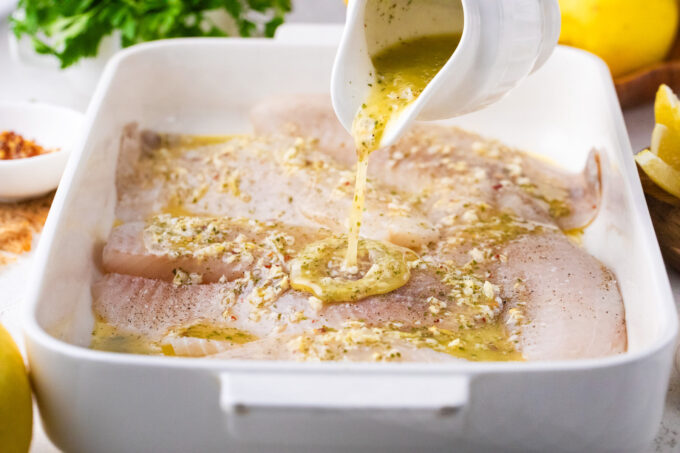 Pouring garlic lemon butter sauce over tilapia fish fillets.