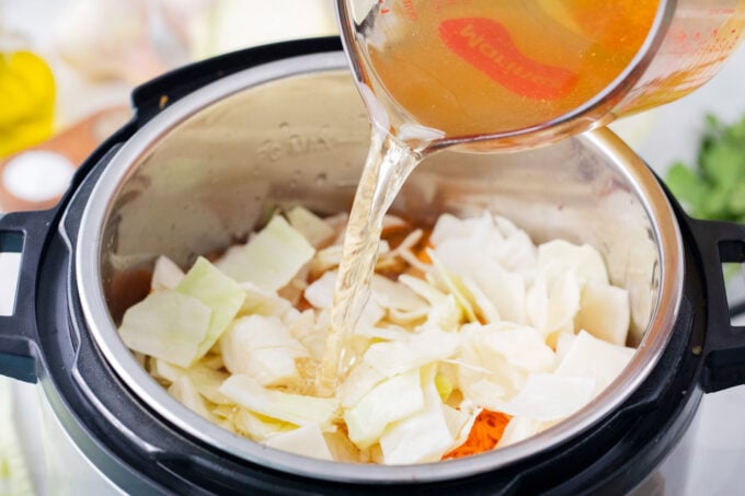 Pouring broth over cabbage in the Instant Pot.