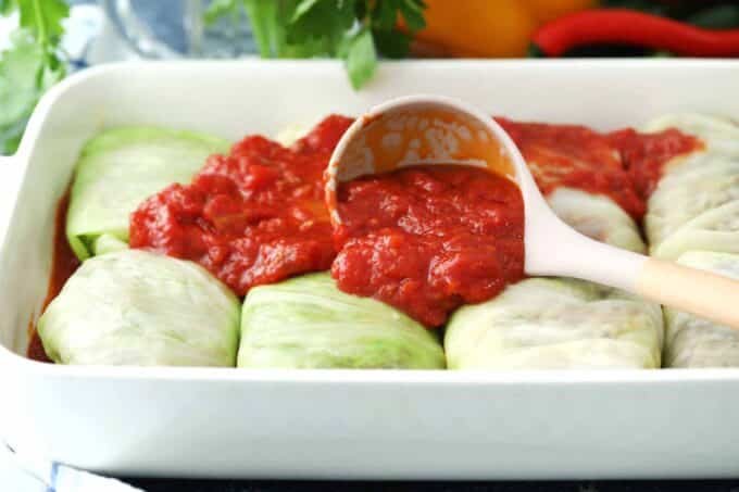 topping cabbage rolls with tomato sauce in a baking dish