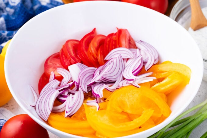 Sliced red tomatoes, yellow tomatoes and red onion in a bowl.
