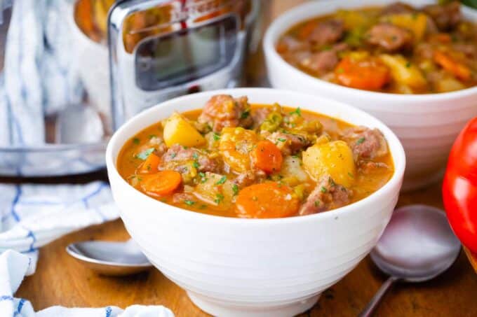 bowls of hearty slow cooker pork stew with a slow cooker next to them