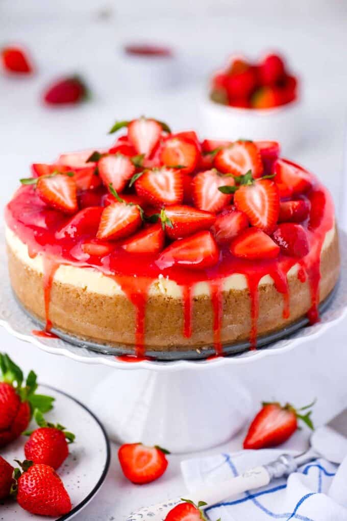 strawberry cheesecake topped with strawberry sauce topping and fresh strawberries on a cake stand