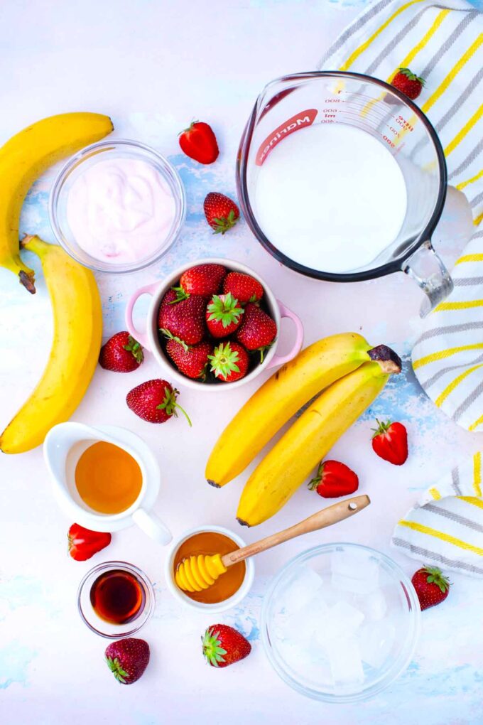 Strawberry banana smoothie ingredients in bowls on a table.