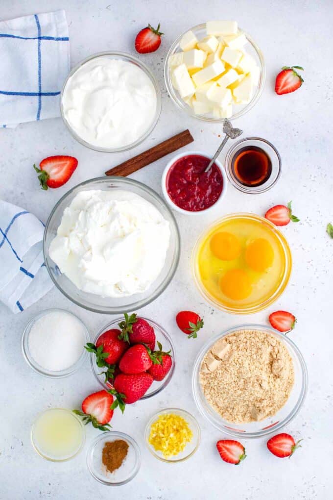 overhead shot of strawberry cheesecake ingredients in bowls on a white surface