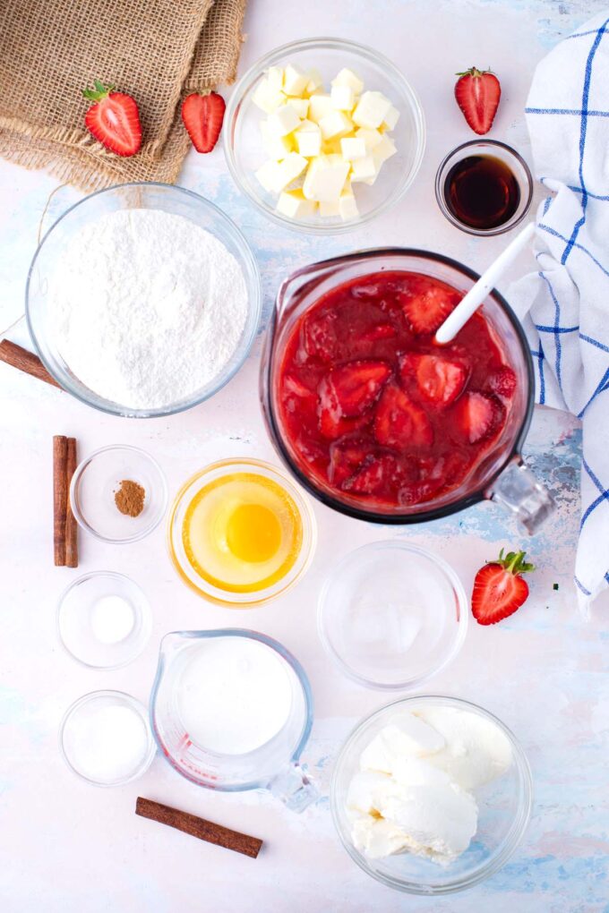 Overhead shot of strawberry cheesecake pie ingredients in bowls on a table.