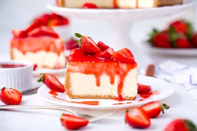 a slice of strawberry cheesecake topped with strawberry sauce topping and fresh strawberries on a plate