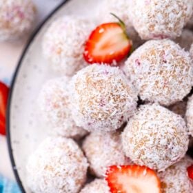 overhead shot of a pile of strawberry coconut truffles covered in shredded coconut and a few sliced strawberries