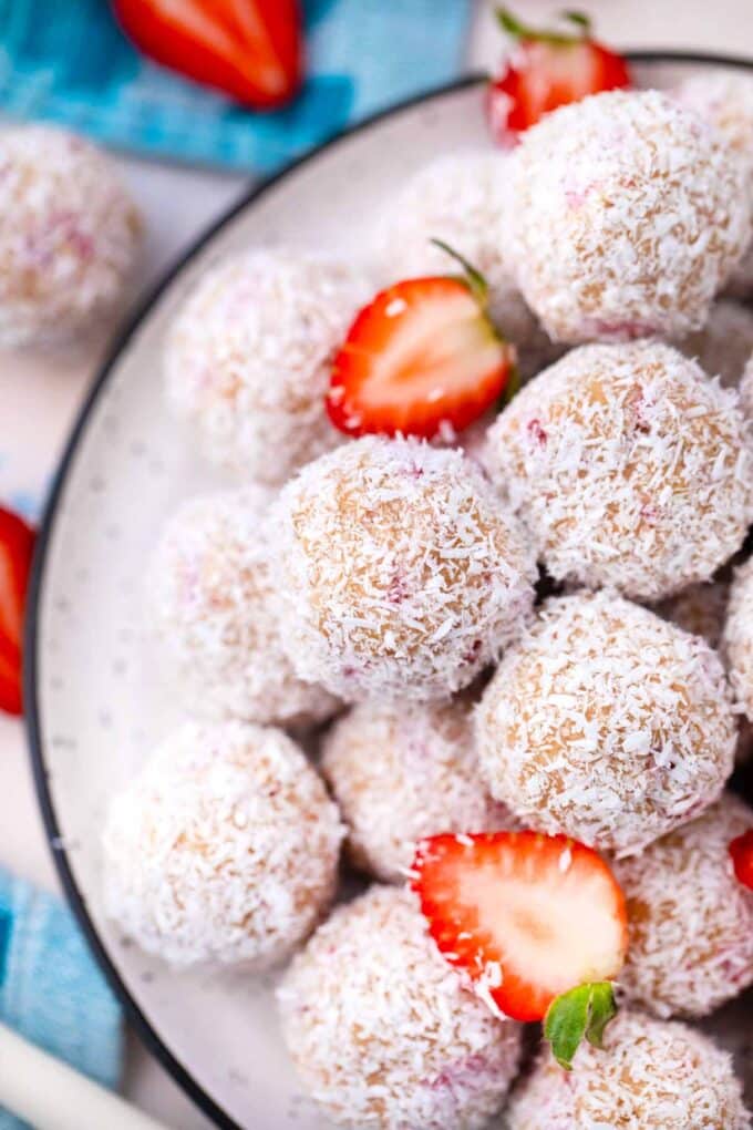 overhead shot of a pile of strawberry coconut truffles covered in shredded coconut and a few sliced strawberries