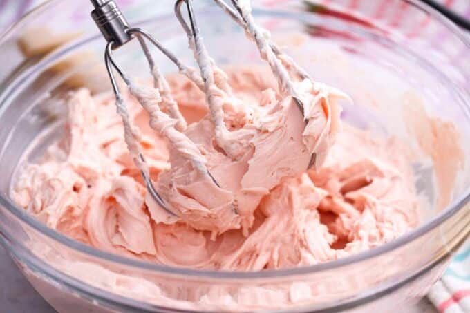Whisking strawberry mascarpone frosting in a bowl.