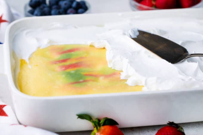 Topping red, white, and blue poke cake with whipped topping.