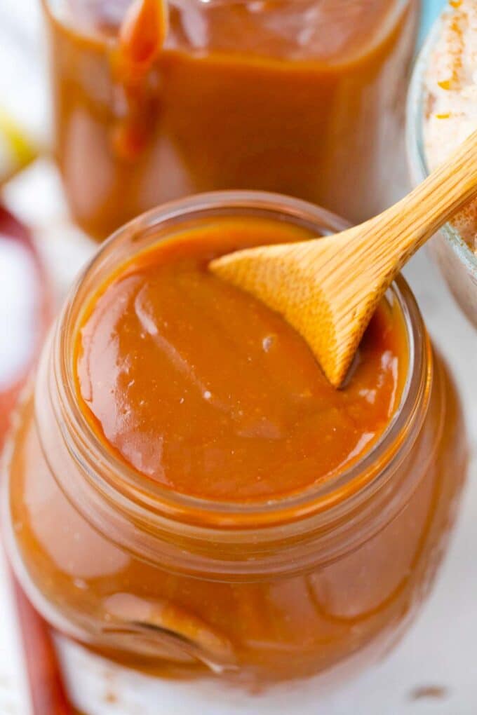 a jar with thick homemade caramel sauce and a small serving wooden spoon in it