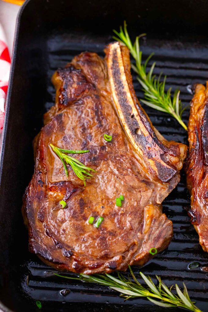 Overhead shot of Asian style grilled rib-eye steak in a grill pan with rosemary.