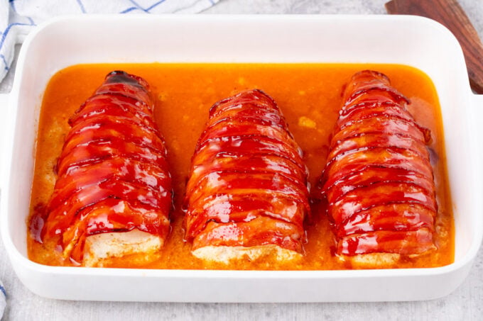 Crispy bacon wrapped cream cheese stuffed chicken in a baking pan.