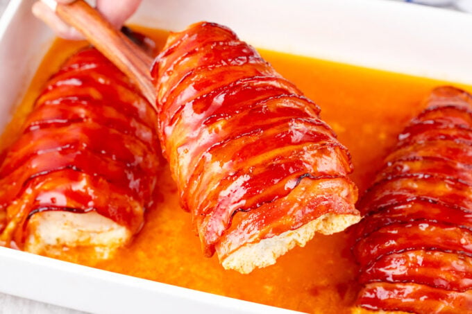 Juicy bacon wrapped cream cheese stuffed chicken in a baking pan.