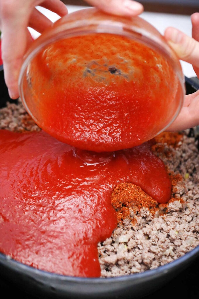 Adding tomato sauce to ground beef.